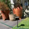 Garden spike deflects a garden hose from a group of pots.